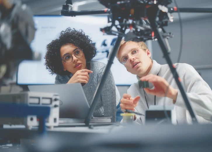 Researchers collaborating in innovation lab, studying drone components and discussing technical details